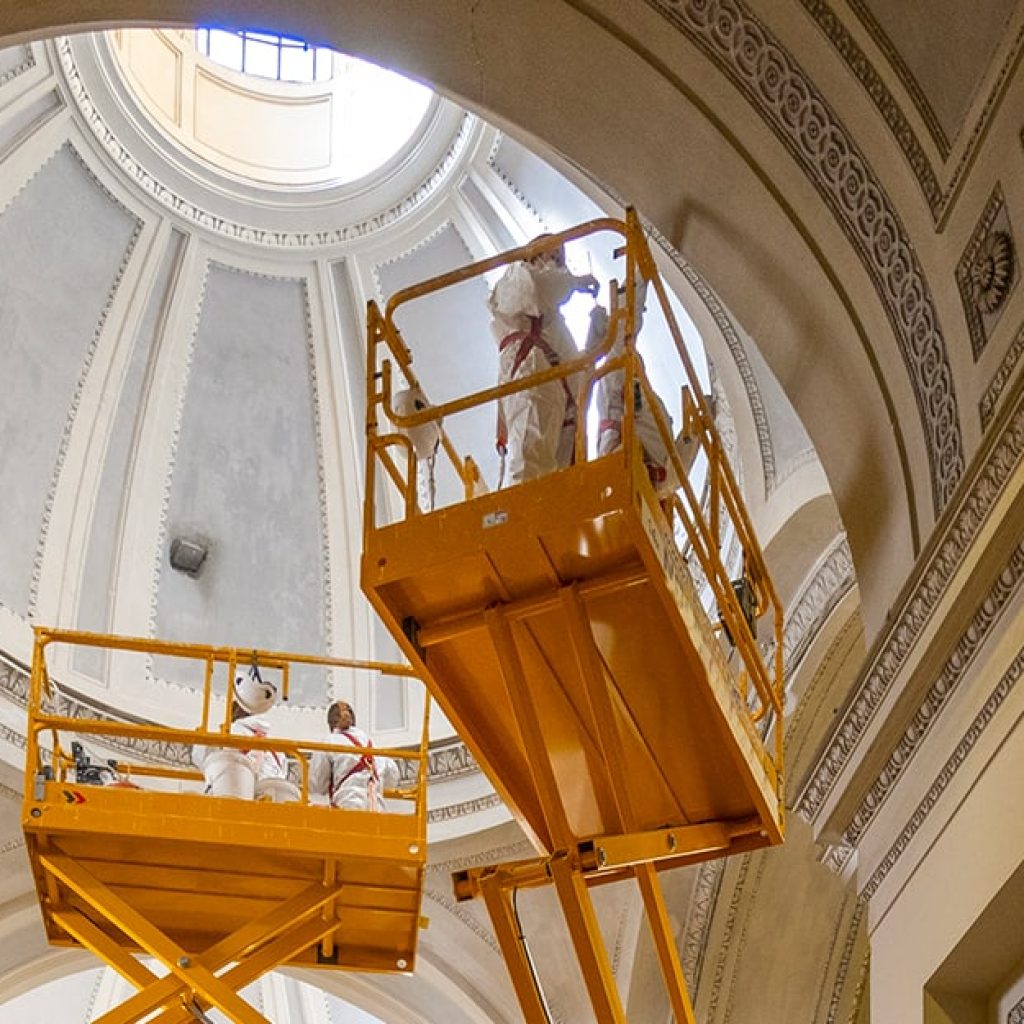 Dei restauratori stanno compiendo dei lavori di restauro in una chiesa su due ponteggi