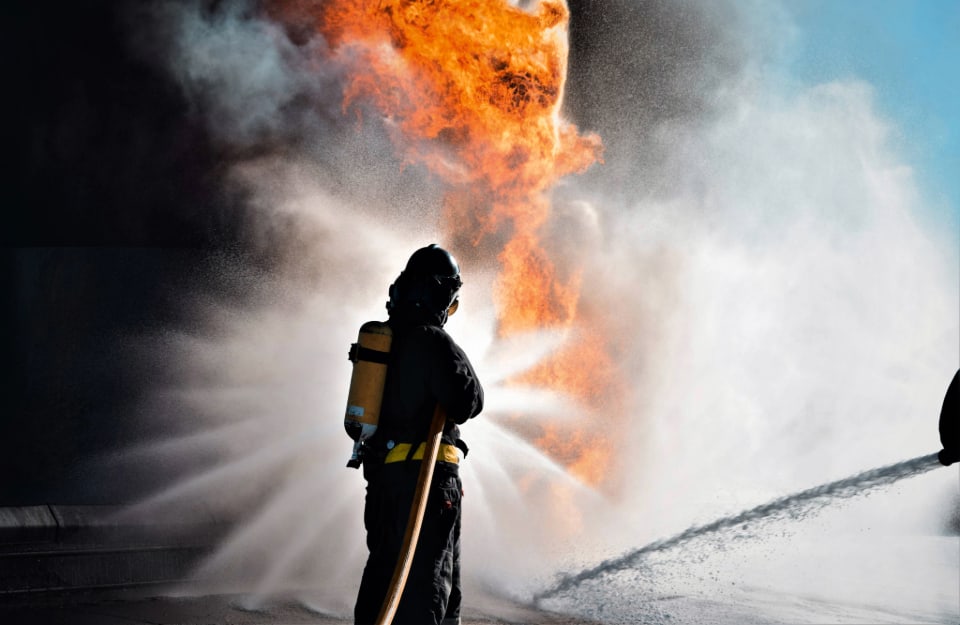 Un pompiere visto di spalle sta cercando di domare un incendio con un getto d'acqua